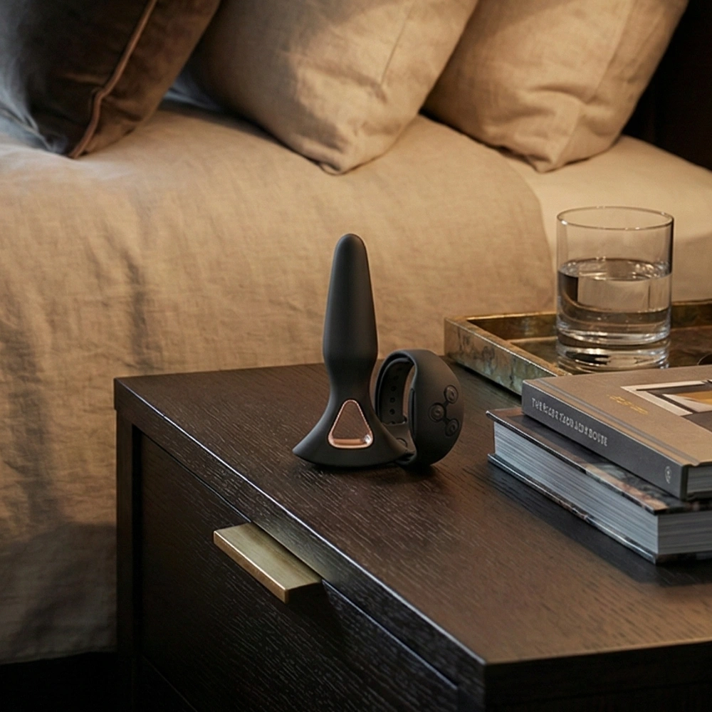 Sextoy anal discret et élégant posé sur une table de chevet à côté d'un lit.