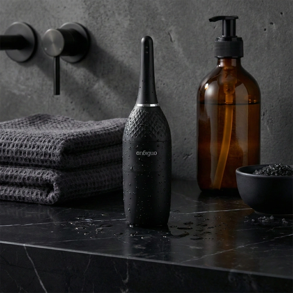 Poire de lavement automatique étanche posée sur un plan en marbre noir avec gouttes d'eau.